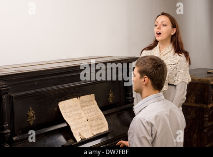 Coppia giovane dando un recital di canto con un attraente femmina giovane cantante accompagnato al pianoforte da un giovane uomo Foto Stock