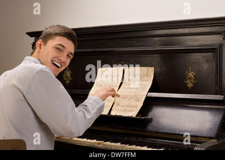 Giovane uomo a ridere come egli siede a suonare il pianoforte svolta a guardare la fotocamera in allegria come egli gode di se stesso Foto Stock