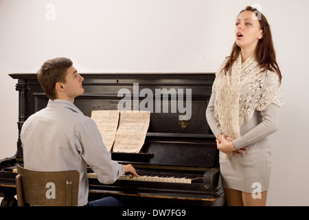 Elegante giovane donna dando un canto classico recital accompagnata su un pianoforte verticale da un bel giovane Foto Stock