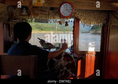 Capitano la sterzatura di un 'slow' in barca sul fiume Mekong in Laos. Foto Stock