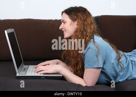 Una giovane donna è sdraiato su un divano e usando il suo computer portatile Foto Stock