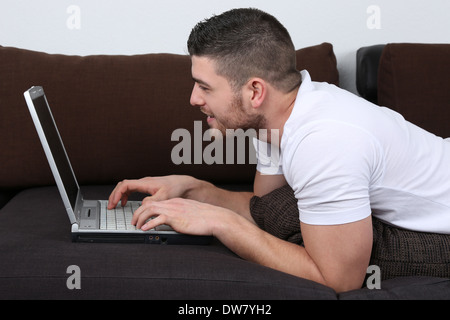 Un giovane uomo è sdraiato su un divano e usando il suo computer portatile Foto Stock