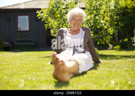 Felice elder donna seduta rilassato su erba in giardino nel cortile e guardando la telecamera sorridendo - all'aperto Foto Stock