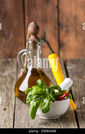 Il basilico fresco con l'annata bottiglia di olio di oliva e giallo peperoncino sul vecchio tavolo in legno Foto Stock