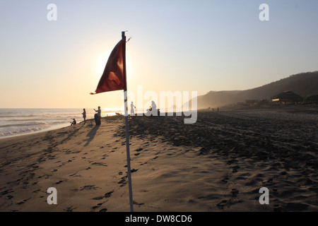 Tramonto sulla spiaggia Mermejita con qualche villeggiante giocando nei pressi di una bandiera rossa, Mazunte, S. Oaxaca, Messico Foto Stock