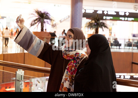 Due musulmani arabi le donne che prendono un selfie su un telefono cellulare, il centro commerciale di Dubai, Emirati Arabi Uniti, Emirati Arabi Uniti Medio Oriente Foto Stock