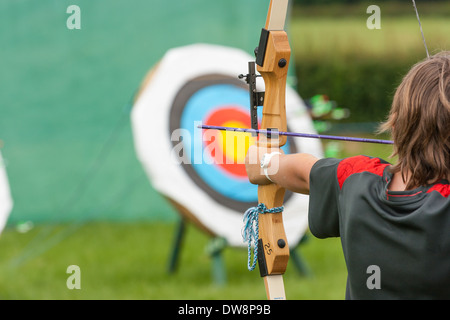 Giovane ragazzo sconosciuto con un lungo arco e frecce tenendo aim e circa a sparare a un bersaglio Foto Stock