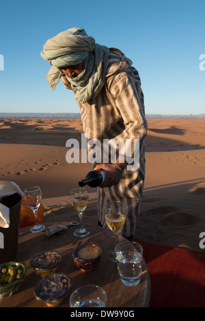 Il Tuareg uomo versando il vino in wineglass presso Erg Chigaga Luxury Desert Camp nel deserto del Sahara, Souss-Massa-Draa, Marocco Foto Stock