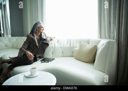 Ritratto di donna matura reclinata su bianco divano di lusso Foto Stock