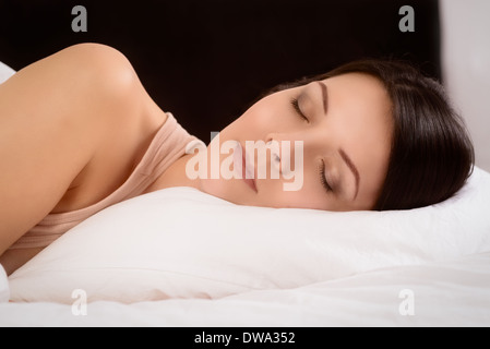 Attraente giovane donna godendo un tranquillo sonno nascosto fino a letto a sognare con un espressione serena Foto Stock