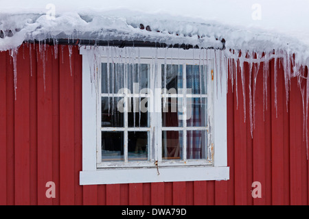 Ghiaccioli appesi da grondaia congelati nella parte anteriore della finestra di legno rosso cabina in inverno, Scandinavia Foto Stock