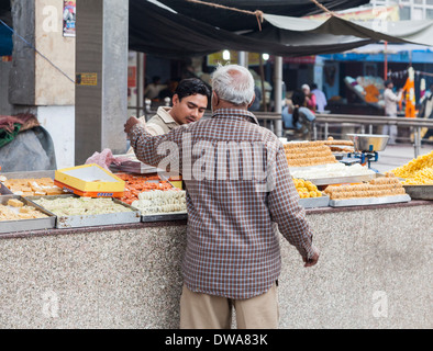 Anziani locale indiana uomo acquisto dolci Indiano da un negozio su strada a Nuova Delhi, India Foto Stock