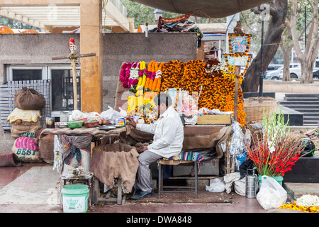 Locale uomo indiano al fiore di strada stallo in New Delhi, India, per la vendita di fiori e ghirlande per un tempio indù offerte Foto Stock