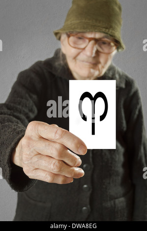 Donna anziana tenendo la scheda con stampa oroscopo ARIETE segno. Il fuoco selettivo sulla carta e le dita. Foto Stock