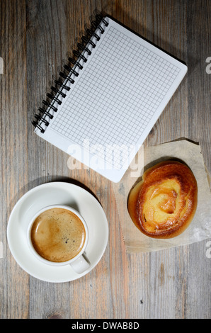 Tazza di caffè espresso, notebook a scacchi e bun su sfondo di legno Foto Stock