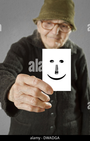 Donna anziana tenendo la scheda stampata con emoticon felice. Il fuoco selettivo sulla carta e le dita. Foto Stock