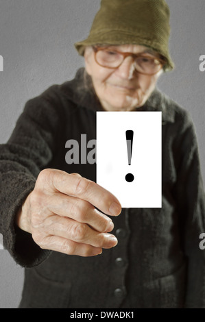 Donna anziana tenendo la scheda stampata con un punto esclamativo. Il fuoco selettivo sulla carta e le dita. Foto Stock