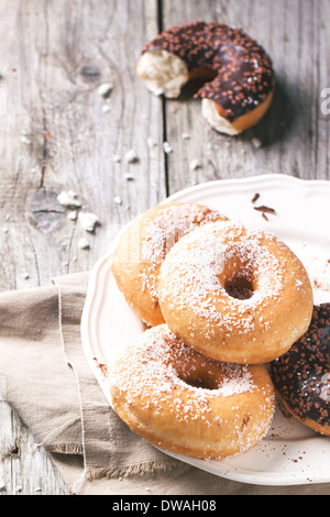 Piastra bianca di ciambelle di zucchero e metà della ciambella di cioccolato servita su un tavolo di legno. Foto Stock