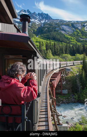 Fotografare passeggeri sullo storico Pass bianco Yukon Route convoglio ferroviario, come si attraversa un ponte, vicino Skagway, Alaska Foto Stock