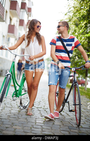 Ritratto di ragazza e ragazzo con biciclette passeggiate verso park e parlare Foto Stock