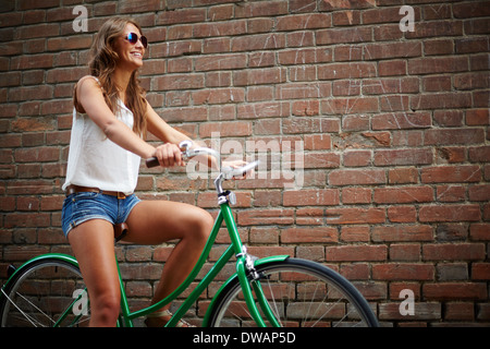 Ritratto di giovane donna equitazione Bicicletta contro un muro di mattoni Foto Stock