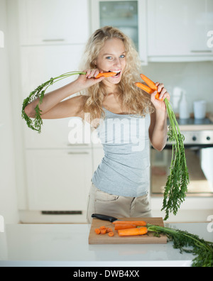 Donna di mangiare la carota a banco di cucina Foto Stock