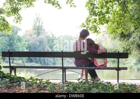 Vista posteriore della romantica coppia giovane seduto sul banco a Lakeside Foto Stock