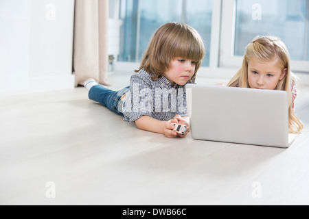 Fratello e Sorella utilizzando laptop sul pavimento a casa Foto Stock