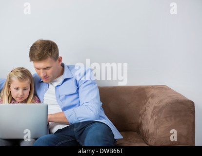 Padre e figlia utilizzando laptop insieme sul divano di casa Foto Stock