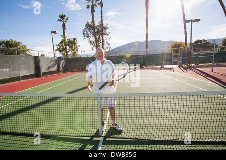 Ritratto di senior giocatore di tennis offrendo handshake su corte Foto Stock