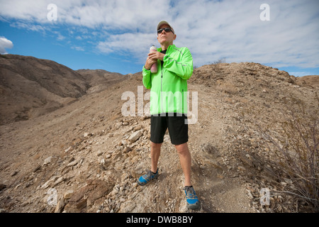 Determinato senior man tenendo la bottiglia di acqua mentre si sta in piedi sul monte Foto Stock