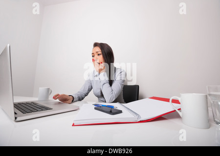 Assonnato imprenditrice lavorando sul portatile in ufficio Foto Stock