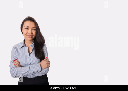 Ritratto di fiducioso imprenditrice in piedi con le braccia incrociate contro uno sfondo grigio Foto Stock
