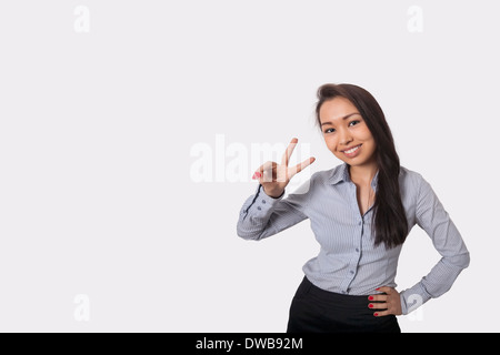 Ritratto di felice imprenditrice che mostra segno di vittoria contro uno sfondo grigio Foto Stock