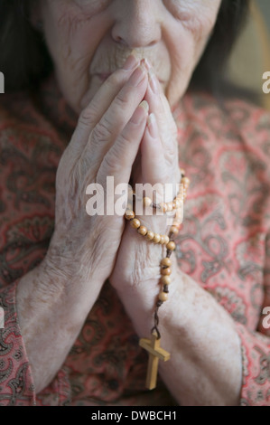 Senior donna orante con il rosario Foto Stock