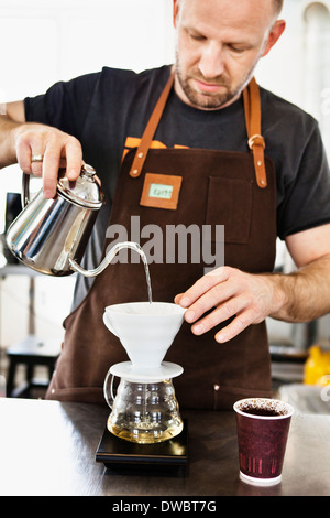 Barista maschio versando acqua bollente in un filtro del caffè Foto Stock