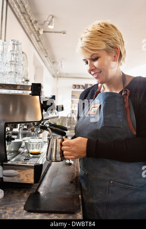 Barista riscaldando latte utilizzando la macchina per il caffè Foto Stock