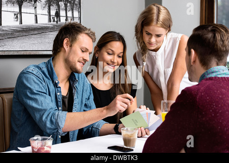 Quattro giovani amici adulti seduti in cafe guardando le carte Foto Stock