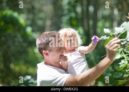 Padre con baby girl spiumatura fiori nella foresta Foto Stock