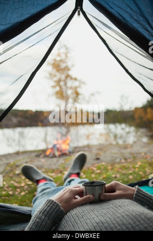 Sezione bassa dell uomo con tazza di caffè mentre giaceva in tenda Foto Stock