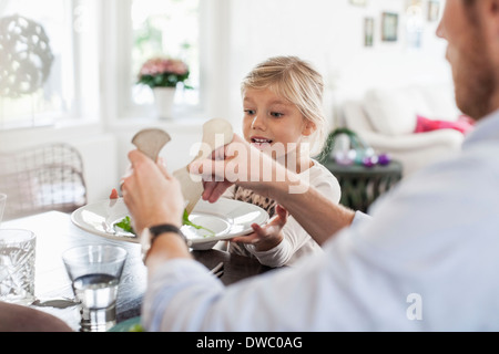 Padre servire insalata alla figlia al tavolo da pranzo Foto Stock