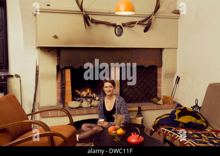 Ritratto di giovane donna seduta sul pavimento accanto al caminetto Foto Stock