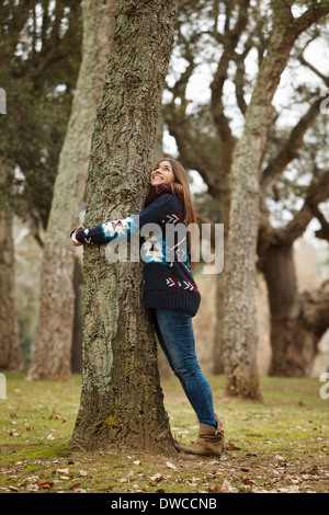 Giovane donna abbracciando albero nella foresta Foto Stock