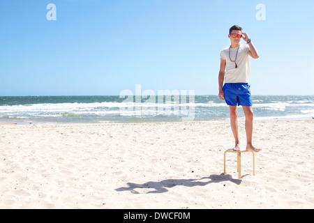 Giovane uomo che pongono sulla sommità di uno sgabello sulla spiaggia, il Port Melbourne, Melbourne, Australia Foto Stock