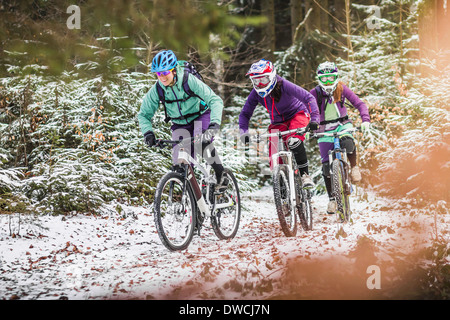 Tre donne appassionati di mountain bike a cavallo attraverso la foresta nella neve Foto Stock