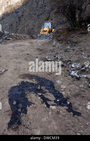 Escavatore e schizzi di olio motore su una controversa nuova strada nella valle Tsum, Nepal. Foto Stock