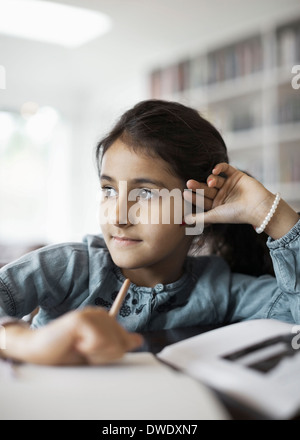 Ragazza che guarda lontano mentre lo studio a casa Foto Stock