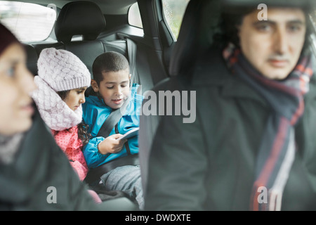 I fratelli con tavoletta digitale mentre si è in viaggio con i genitori Foto Stock