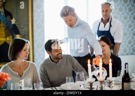 Cameriere che serve acqua per la gente di affari presso il ristorante con chef in piedi in background Foto Stock