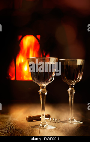 Due bicchieri di vino rosso da uno scoppiettante fuoco di registro Foto Stock